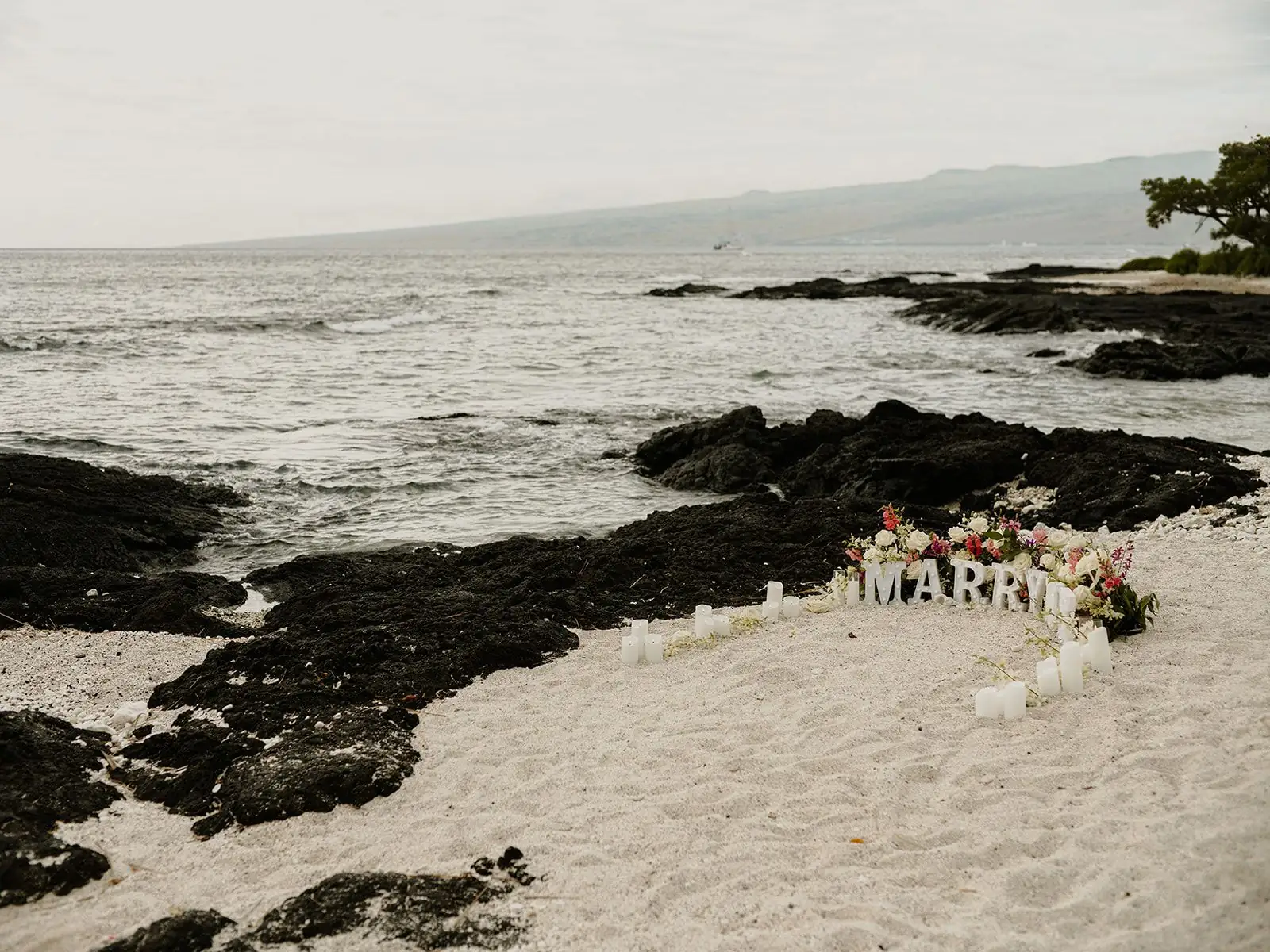 A flower-filled Marry Me setup on a quiet black-lava beach